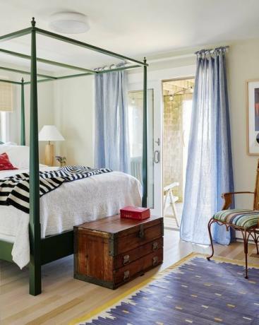 υπνοδωμάτιο επισκεπτών, λευκό λινό και πράσινο πλαίσιο κρεβατιού με κίτρινο και μπλε χαλί με καφέ ξύλινο στήθος