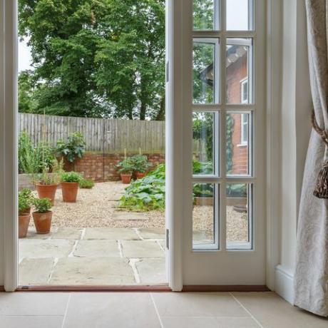 θέα στον κήπο από το εσωτερικό του σπιτιού με γαλλικές πόρτες που οδηγούν σε μια αυλή στον κήπο της κουζίνας