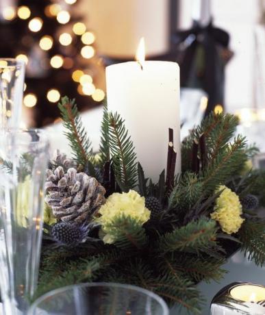 ασπρόμαυρα χριστουγεννιάτικα στολίδια με ασημί και φρέσκα βιολέτα για το σπίτι, τραπέζι φαγητού με κεντρικό κερί από φρέσκο ​​κομμένο κλαδί, κουκουνάρια και γαρύφαλλα