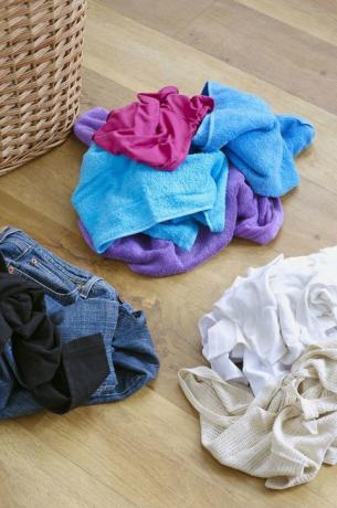 Βρώμικα ρούχα χωρίζονται σε σωρούς σε ξύλινο πάτωμα δίπλα στο καλάθι πλυντηρίων