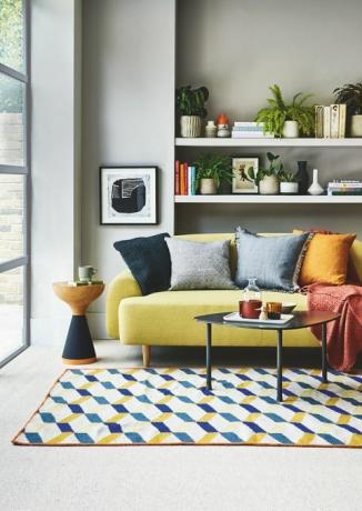 καθιστικό, κίτρινο καναπέ άσπρο ράφι πίσω με ένα μπλε και κίτρινο χαλί με μοτίβο στο πάτωμα