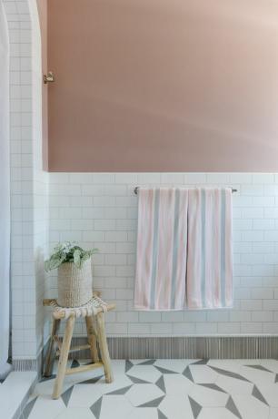 ροζ βαμμένος τοίχος, λευκό κεραμίδι του μετρό, ξύλινο σκαμπό, λευκή κουρτίνα ντους, γεωμετρικά λευκά και γκρι πλακάκια, ροζ και γκρι πετσέτες