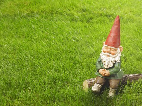 Κήπος gnome με κόκκινο καπέλο κάθεται σε πράσινο γκαζόν