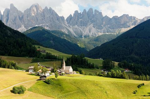 Καλοκαιρινό τοπίο της ειδυλλιακής Val di Funes με τις ανισόπεδες κορυφές της οροσειράς Odle (Geisler) στο βάθος και μια εκκλησία στο χωριό Santa Maddalena στην καταπράσινη χορτώδη κοιλάδα στο Dolomiti, νότιο Τυρόλο, Ιταλία