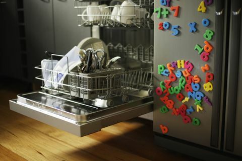 Μηχανή πλυσίματος πιάτων με ανοιχτό συρτάρι δίπλα στο ψυγείο που καλύπτεται από μαγνήτες παιδικών ψυγείων