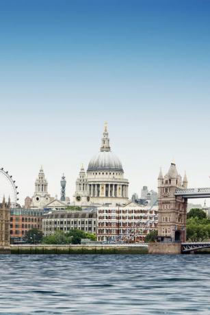 μοντάζ του Λονδίνου ενάντια στον απλό μπλε ουρανό με τον ποταμό Τάμεση σε πρώτο πλάνο