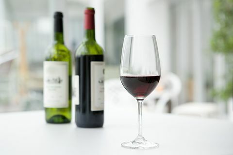 Κόκκινο κρασί σε φιάλες και γυαλί σε λευκό τραπέζι