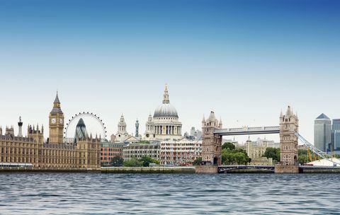 μοντάζ του Λονδίνου ενάντια στον απλό μπλε ουρανό με τον ποταμό Τάμεση στο πρώτο πλάνο