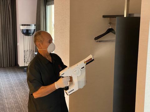 άντρας σε ένα δωμάτιο ξενοδοχείου χρησιμοποιώντας έναν ψεκαστήρα για την απολύμανση της ανοιχτής ντουλάπας